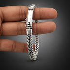 Silver bracelet with braided design held by a hand on a white background