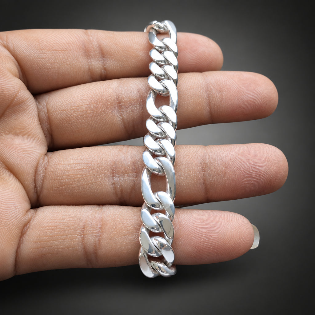 A silver Cuban link chain bracelet held vertically against a person's hand, showing its polished metallic links and dark gray gradient background.