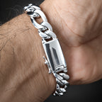 A close-up of a silver-toned chunky chain bracelet with a rectangular clasp, worn on a person's wrist against a dark background.