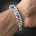 A close-up of a polished silver Cuban link bracelet worn on a person's wrist against a dark gray background.