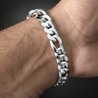 A polished silver Cuban link chain bracelet worn on a person's wrist, shown in a close-up shot against a dark background.