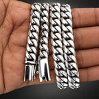 Three silver Cuban link bracelets displayed on a person's hand against a dark gray background.