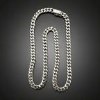A silver-toned Cuban link chain necklace with a lobster clasp, displayed on a dark black background.