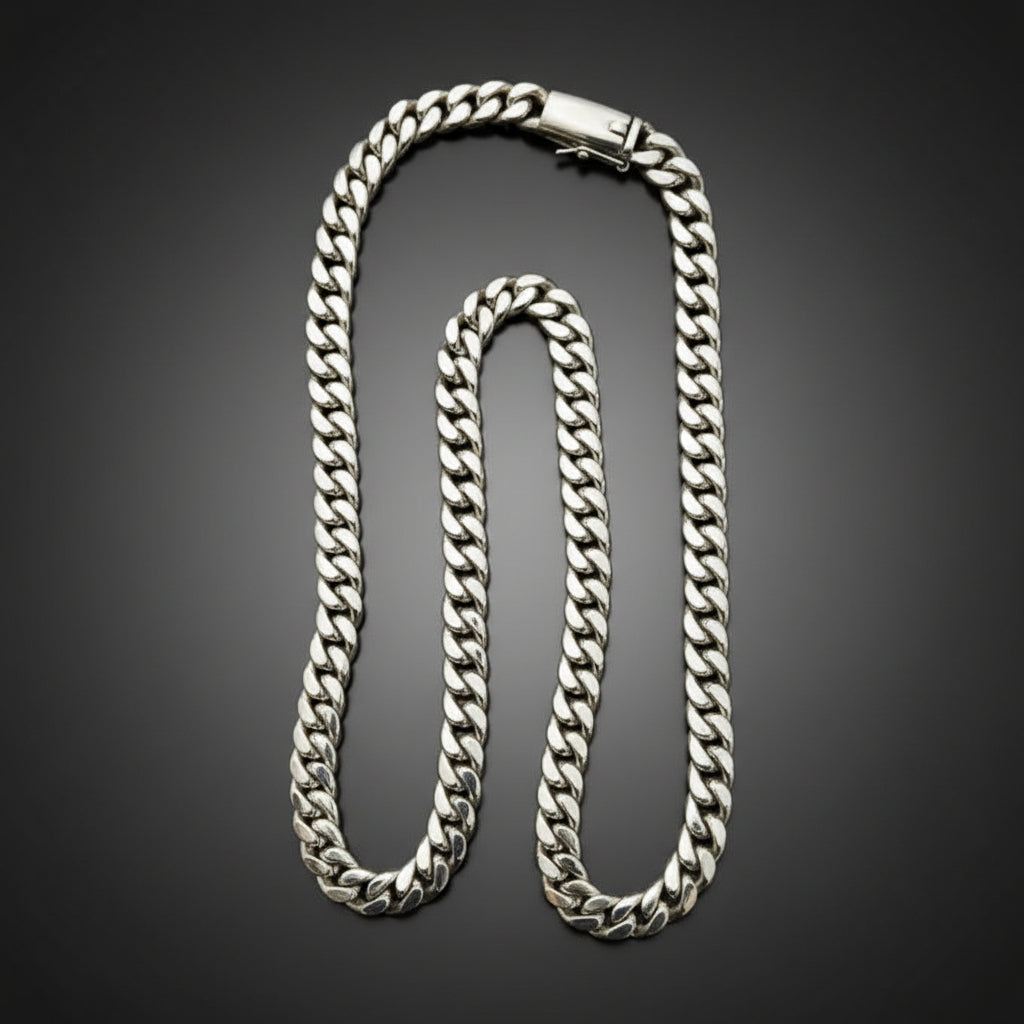 A silver-toned Cuban link chain necklace with a lobster clasp, displayed on a dark black background.