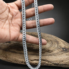 Hand holding a silver chain with a wooden surface in the background