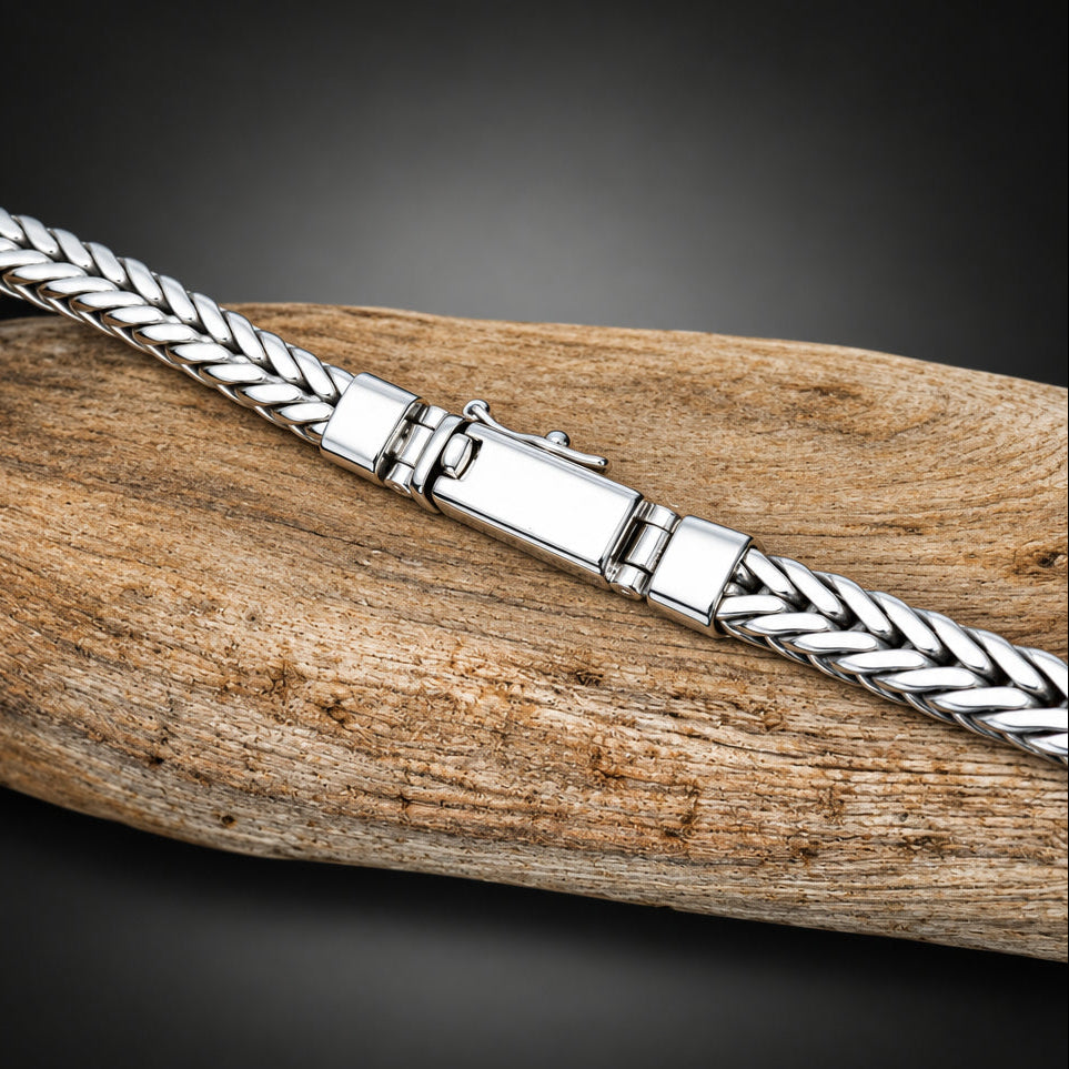 Silver braided bracelet on a wooden surface with a black background
