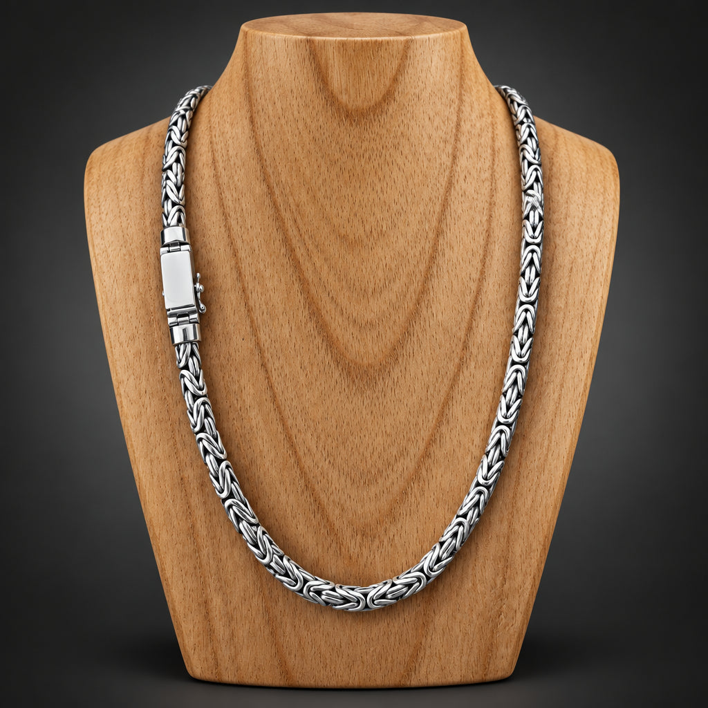 A silver-toned braided chain necklace with a rectangular clasp, displayed on a light brown wooden surface.