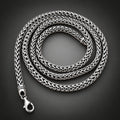 A silver braided chain necklace coiled in a person's hand against a black background.