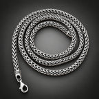 A silver braided chain necklace coiled in a person's hand against a black background.