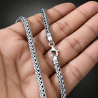 Silver chain necklace held in a hand against a black background