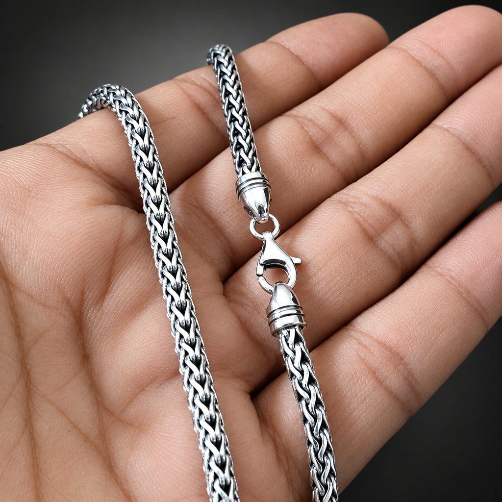 Silver chain necklace held in a hand against a black background