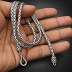 Silver braided necklace with clasp held in a hand against a dark background