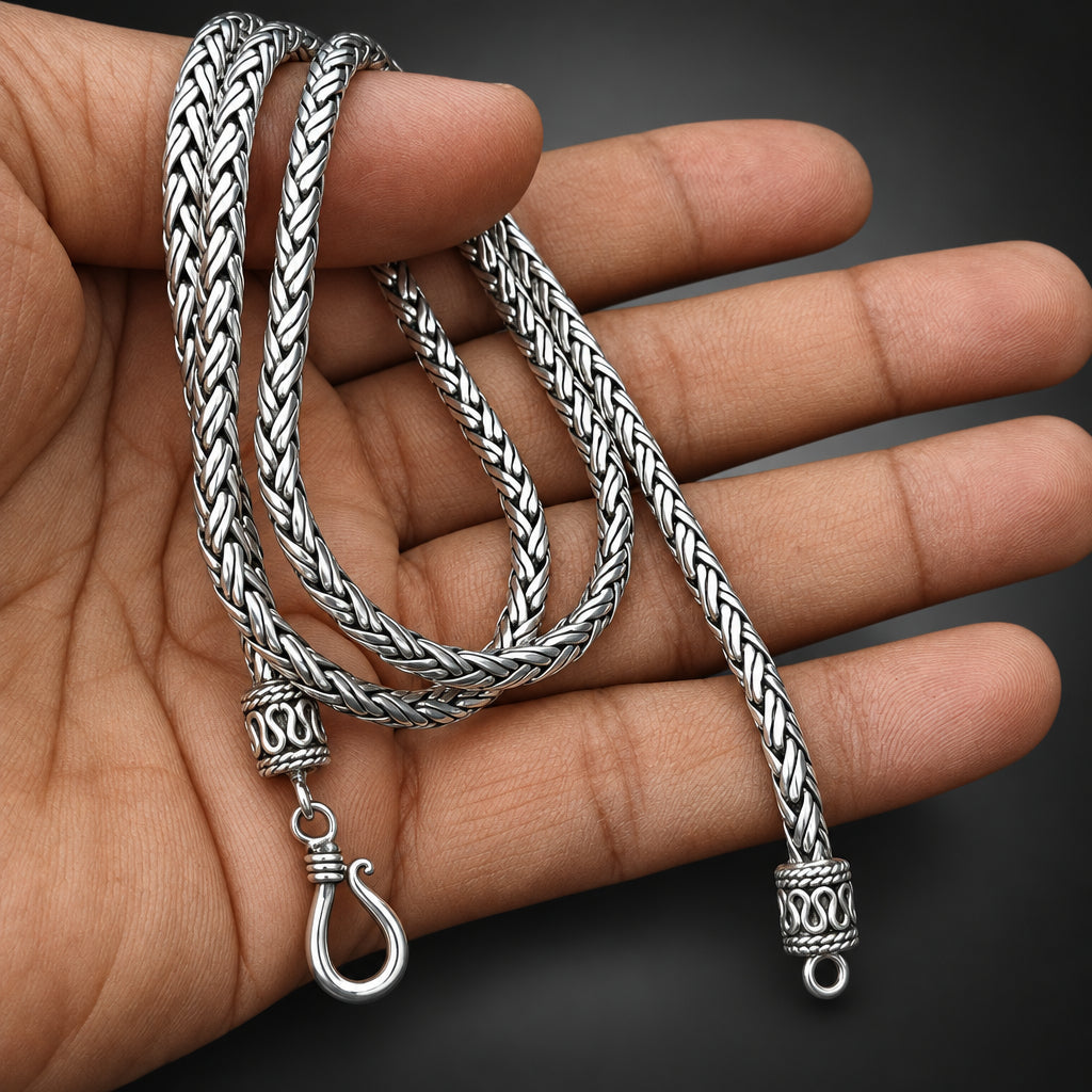 Silver braided necklace with clasp held in a hand against a dark background