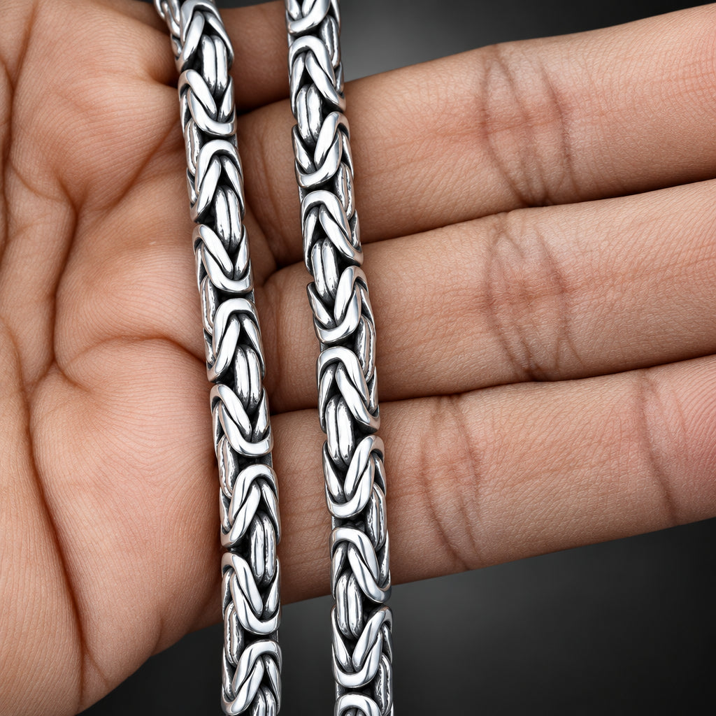 Two silver bracelets with intricate patterns held between fingers.