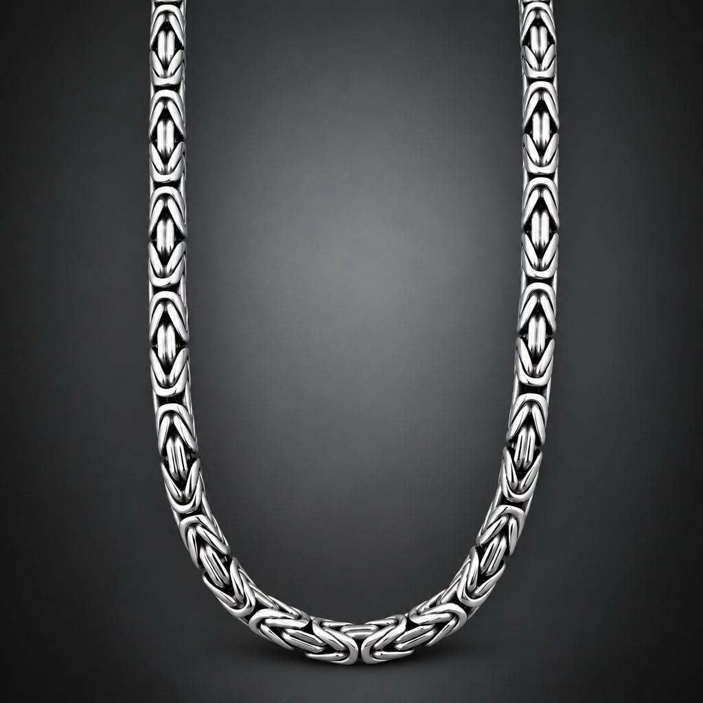 A close-up studio shot of a silver-toned chain necklace with repeating geometric interlocking links, arranged in a U-shape against a dark gray gradient background.