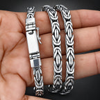 A silver-toned chain bracelet with a textured, interlocking link design, displayed on a person's hand against a black background.