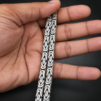Silver bracelet with intricate design held between fingers against a dark background