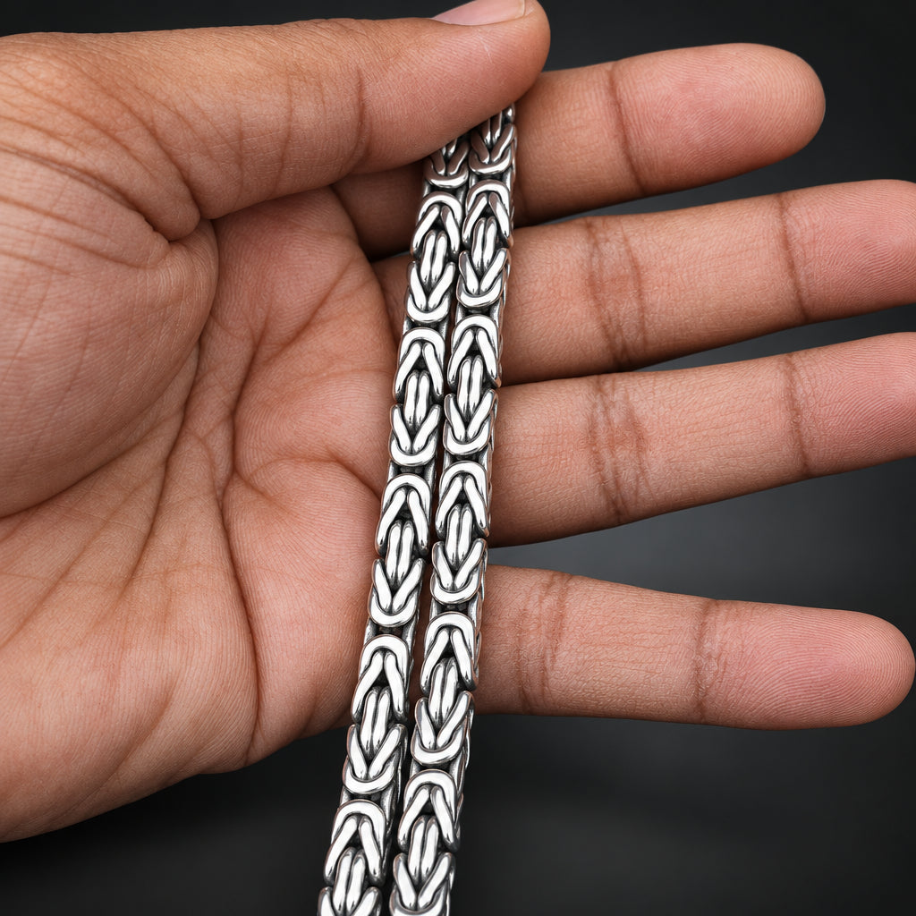 Silver bracelet with intricate design held between fingers against a dark background