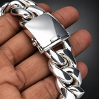 A close-up of a hand holding a chunky silver Cuban link chain bracelet, focusing on the polished metal clasp and links.