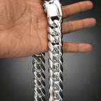A close-up of a hand holding a thick, polished silver Cuban link chain bracelet against a dark gray gradient background.
