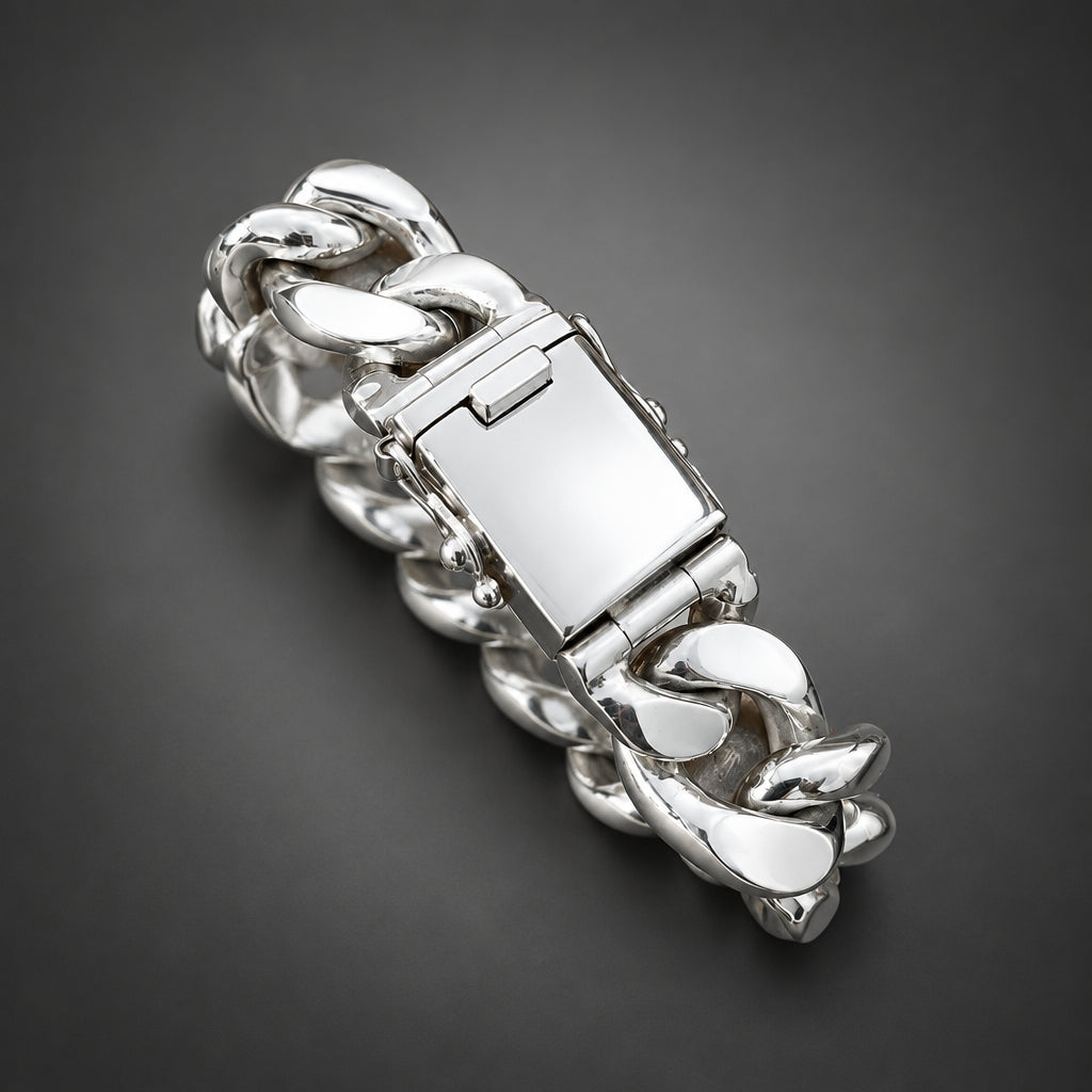 A close-up of a hand holding a chunky silver chain bracelet with a polished rectangular clasp against a neutral gray background.