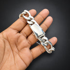 A silver-toned chunky curb link chain bracelet held in a person's hand against a dark background.