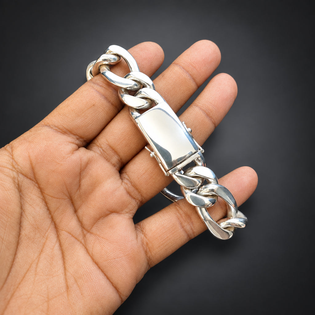 A silver-toned chunky curb link chain bracelet held in a person's hand against a dark background.