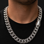 A close-up of a man's neck and chest wearing a thick, polished silver Cuban link chain necklace over a black t-shirt.