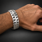 A close-up of a person's wrist wearing a wide, chunky silver-toned chain-link bracelet on a dark wood background.