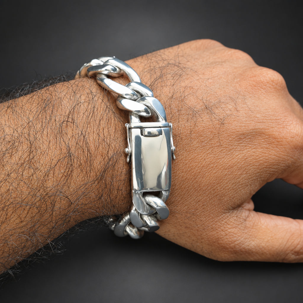A close-up of a person's wrist wearing a chunky silver-tone metal chain bracelet with a rectangular clasp, set against a dark background.