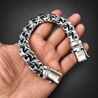 A silver-toned chunky chain link bracelet with a polished clasp, held in a person's hand against a solid black background.