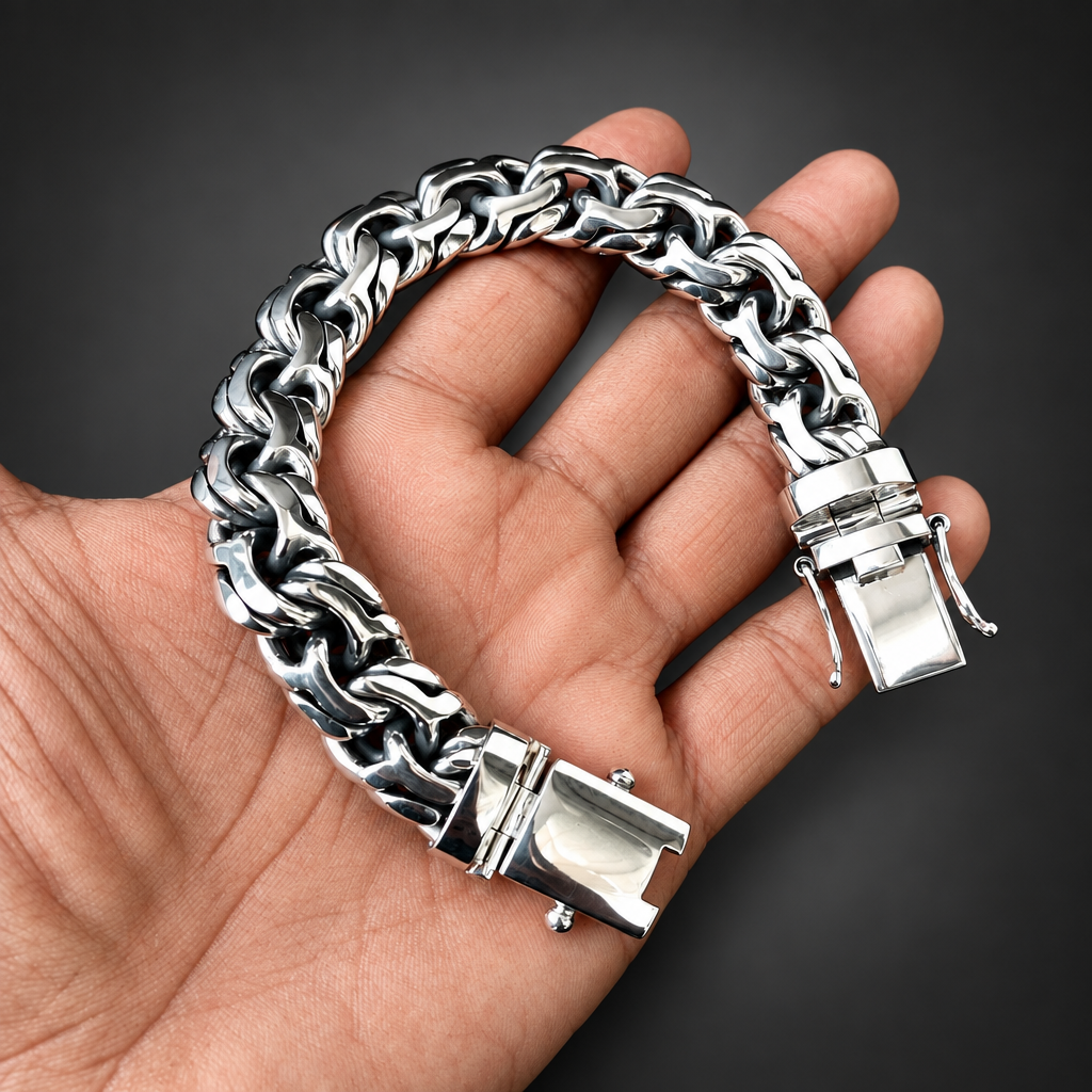 A silver-toned chunky chain link bracelet with a polished clasp, held in a person's hand against a solid black background.