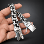 A silver-toned chunky chain bracelet with a unique lock clasp, held in a person's hand against a solid black background.