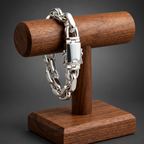 A silver-toned chunky chain bracelet with a rectangular clasp, displayed on a dark wood jewelry stand against a neutral beige background.