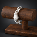 A silver-toned chain bracelet with a padlock clasp, displayed on a dark wood cylindrical stand against a dark gray background.
