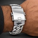 A close-up of a silver stainless steel watch with a wide, polished Cuban link bracelet worn on a person's wrist.