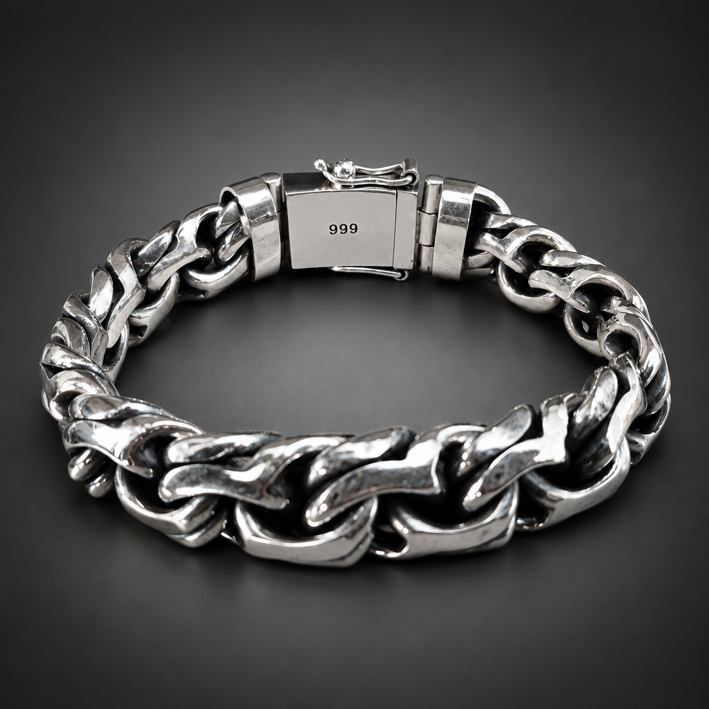 A chunky silver-tone steel chain bracelet with a clasp stamped '999', displayed on a rustic dark wood background.