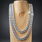 A thick silver Cuban link chain necklace draped over a light wood display stand against a dark background.