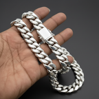 A close-up of a hand holding a thick, polished silver Cuban link chain bracelet against a dark background.