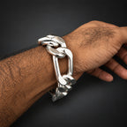 A close-up of a person's hairy wrist wearing a chunky, polished silver chain-link bracelet against a solid black background.