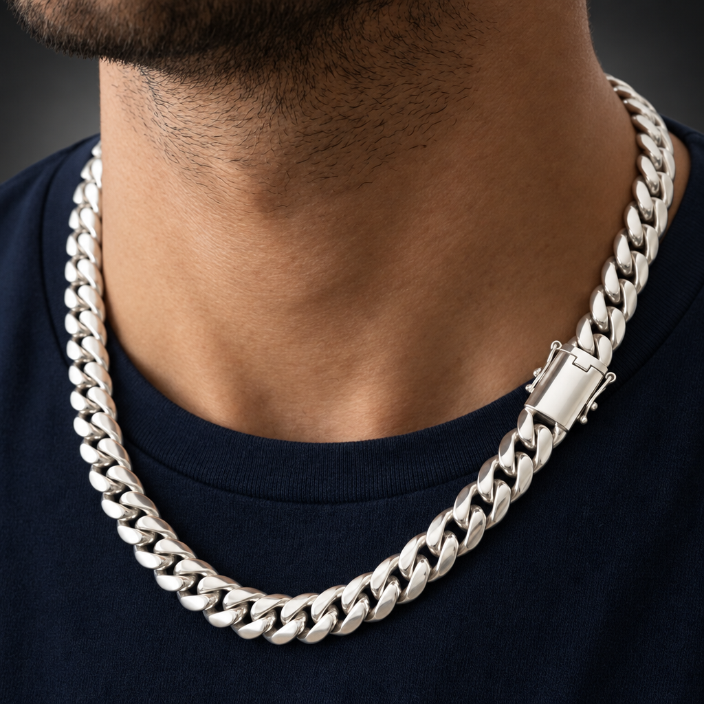 A close-up of a man wearing a thick silver Cuban link chain necklace over a navy blue t-shirt.