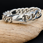 A polished silver-toned chunky curb link bracelet resting on a piece of natural wood against a dark background.
