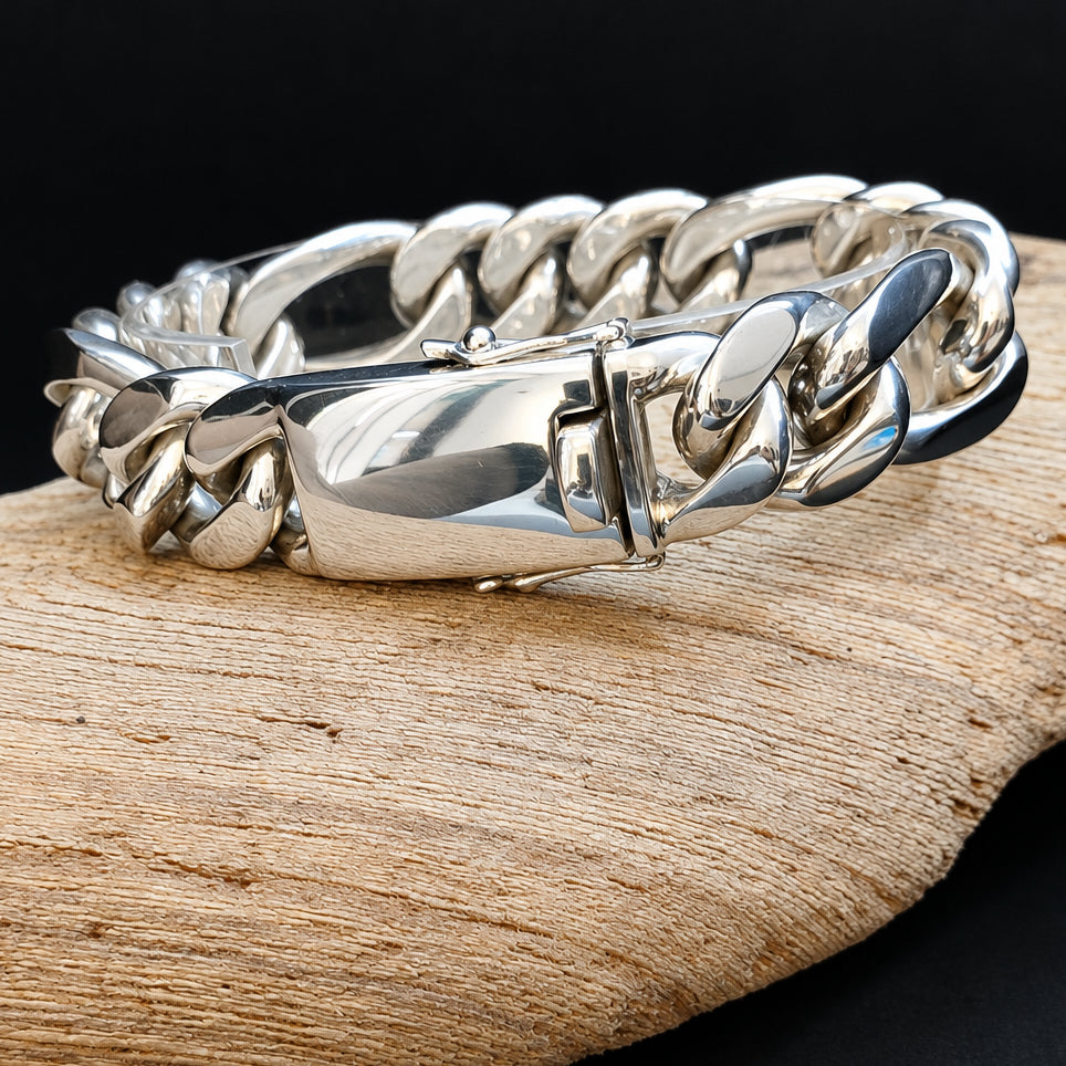 A polished silver-toned chunky curb link bracelet resting on a piece of natural wood against a dark background.