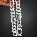 A close-up of a chunky silver Cuban link chain necklace being held by a hand against a solid black background.