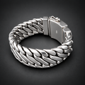 A chunky silver-toned metal bracelet with a woven curb-link design and a rectangular clasp, photographed on a dark gray to black gradient background.